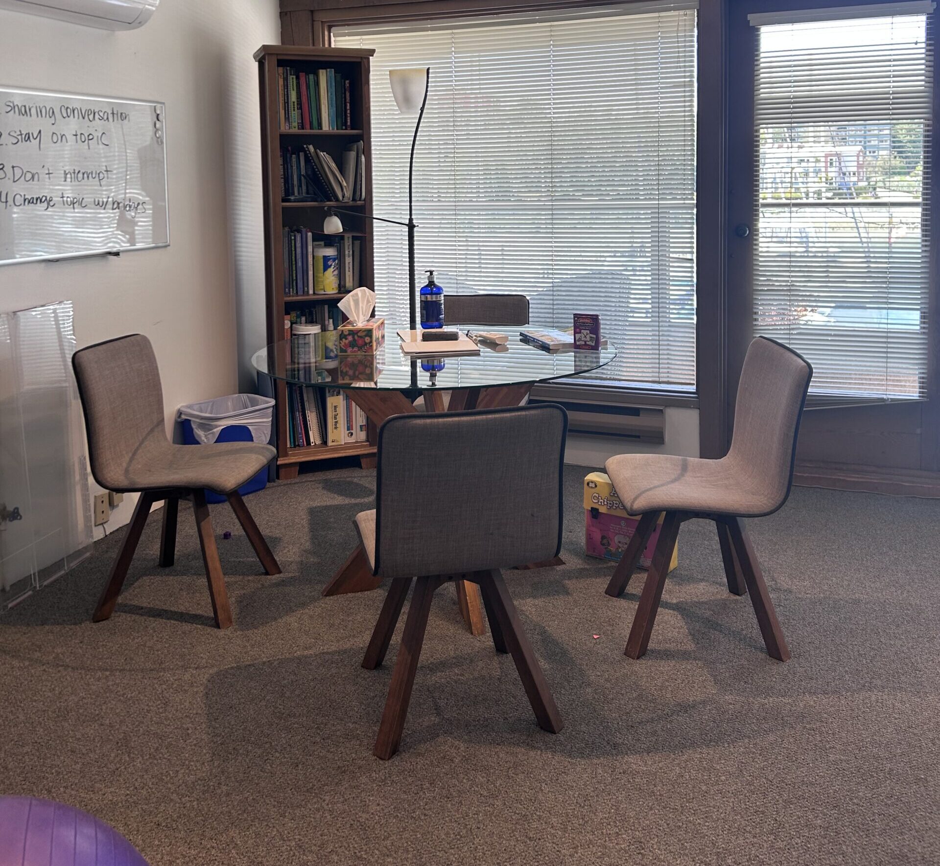 A photo of a table with chairs in the Granville Island Speech clinic and a whiteboard with writing on it.
