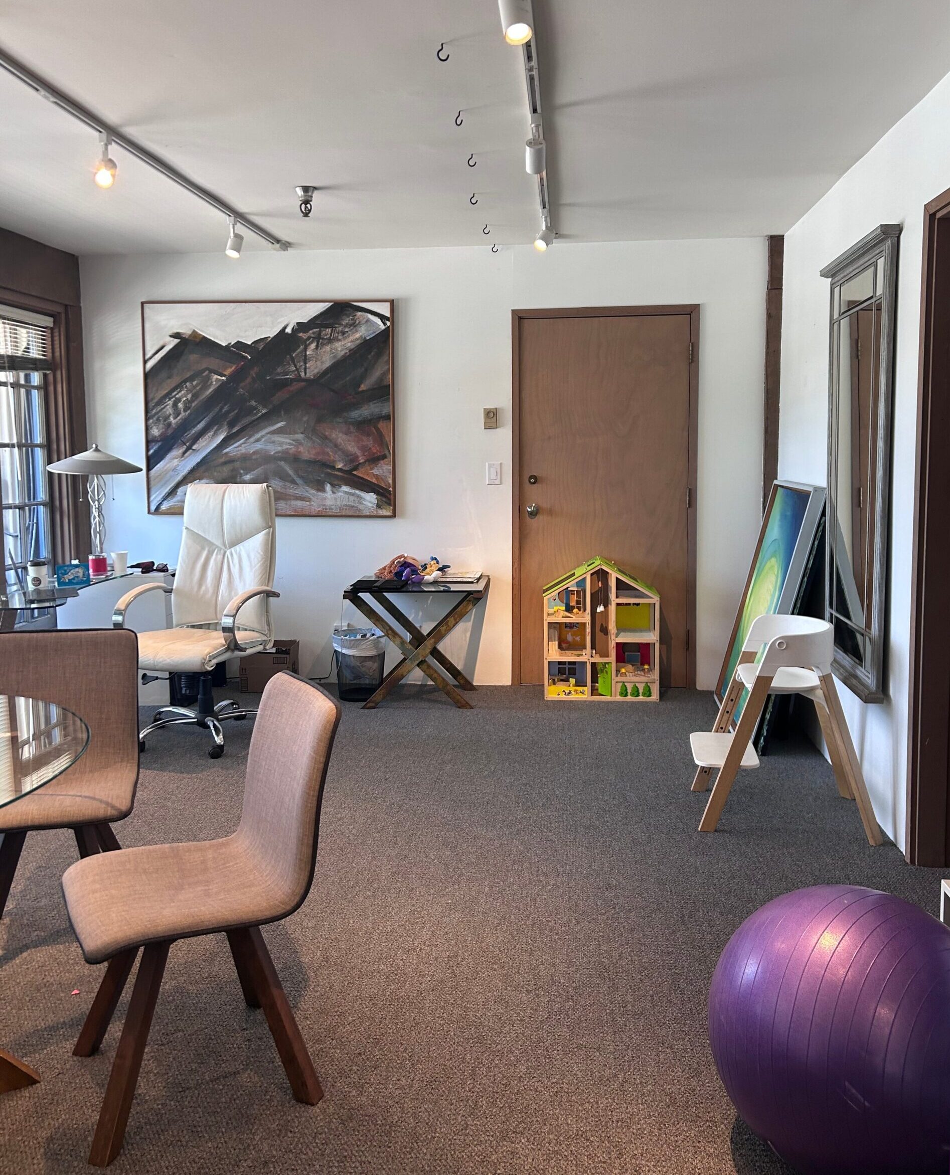 A photo of a room inside the Granville Island Speech clinic. There is a painting on the wall, toys for children, a yoga ball, and a table with chairs.