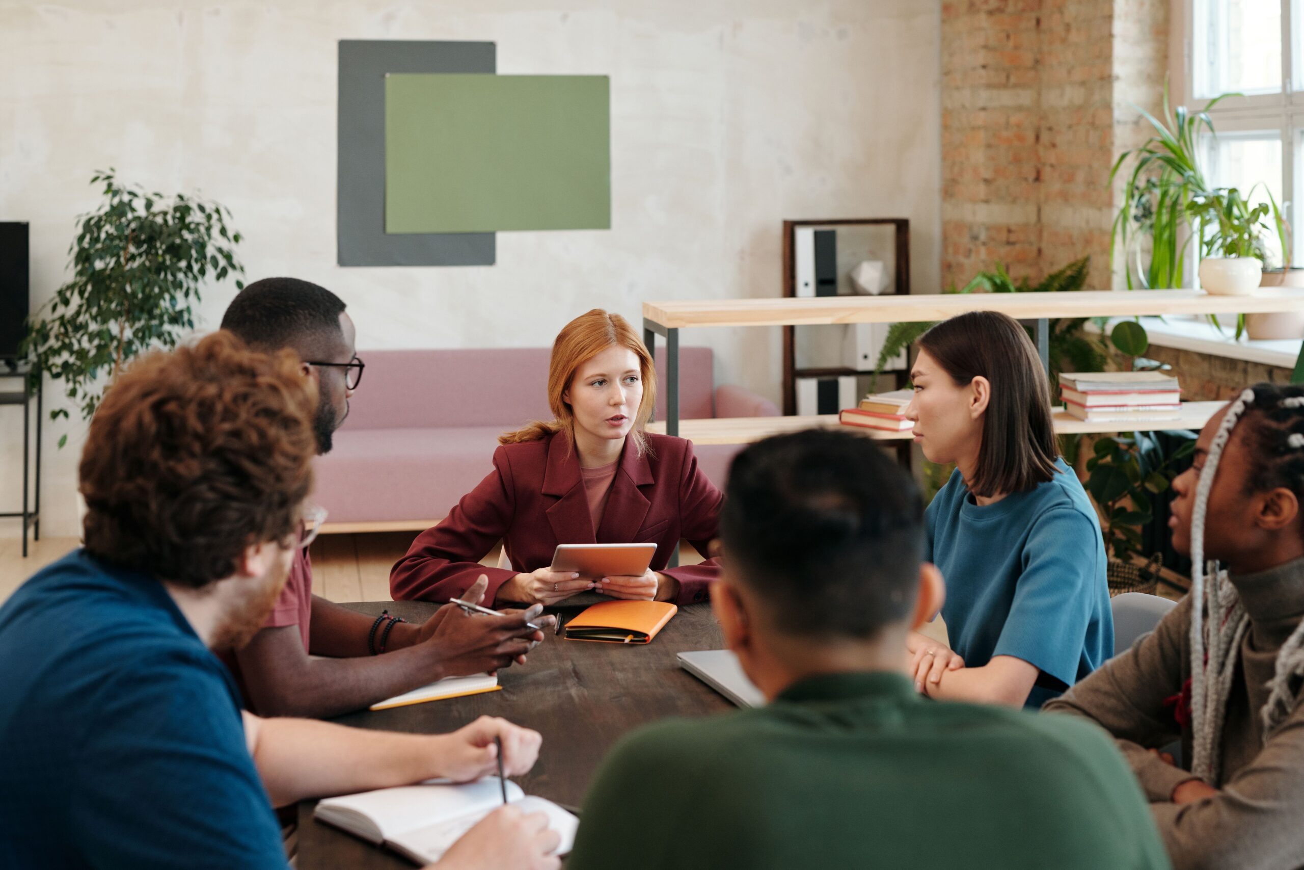A diverse group of women and men are sitting around a table talking to each other.